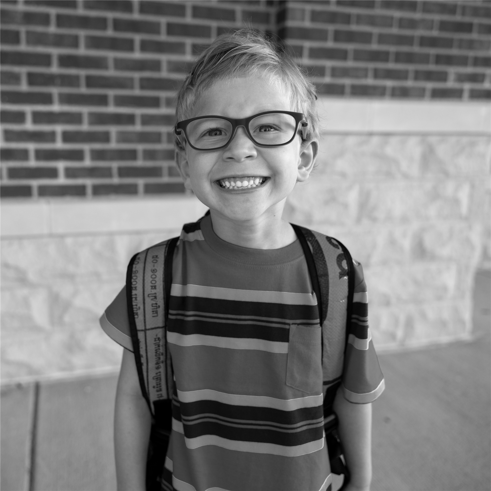 a boy student with a backpack and glasses smiling